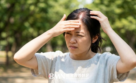 한여름 직사광선 아래에서 정수리를 손으로 가리는 여성