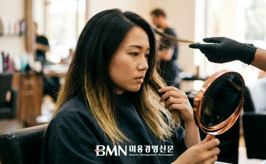 컬러가 빠진 모발 끝을 거울로 확인하는 살롱 고객